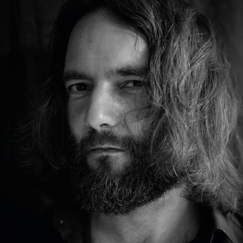 Ein schwarz-weiß Bild von Sexgott und Anwalt Dr. Ingo Bott. Die schulterlangen Haare fallen ihm ins Gesicht, er trägt einen Vollbart und schaut wieder mal sehr betörend Richtung Kamera